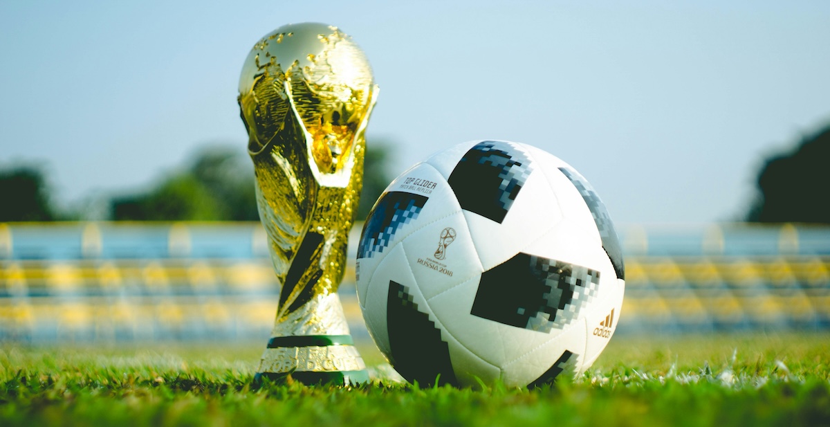 The FIFA World Cup trophy next to a soccer ball on a grass field
