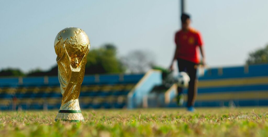 The FIFA World Cup trophy on a grass field with a soccer player